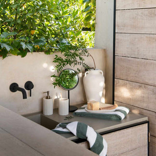 Foto ambiente de casa de banho exterior com o conjunto de copo, doseador e base da gama stripes bege.