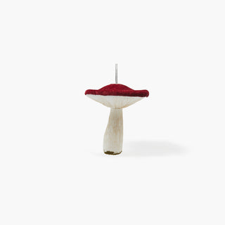 Cogumelo decorativo com chapéu vermelho de textura macia e pé branco, com base de musgo e cordão prateado para pendurar, sobre fundo cinzento claro