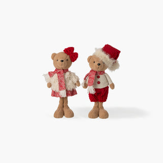 Dois ursinhos de peluche em pé, ela com laço vermelho e vestido às riscas, ele com gorro de pelo, cachecol e calções vermelhos