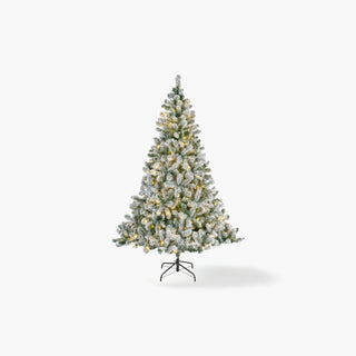 Árvore de Natal artificial com ramos verdes cobertos de neve e pequenas luzes quentes, sobre base de metal e fundo branco