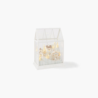 Caixa de vidro em forma de casa com uma vila nevada branca e dourada no interior, iluminada por luzes LED quentes